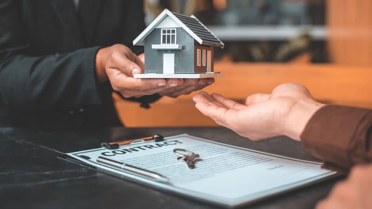 Foto de pessoas na mesa, foco nas suas mãos. Elas passam uma casa em miniatura. Representa justiça arbitral: posso perder meus bens?