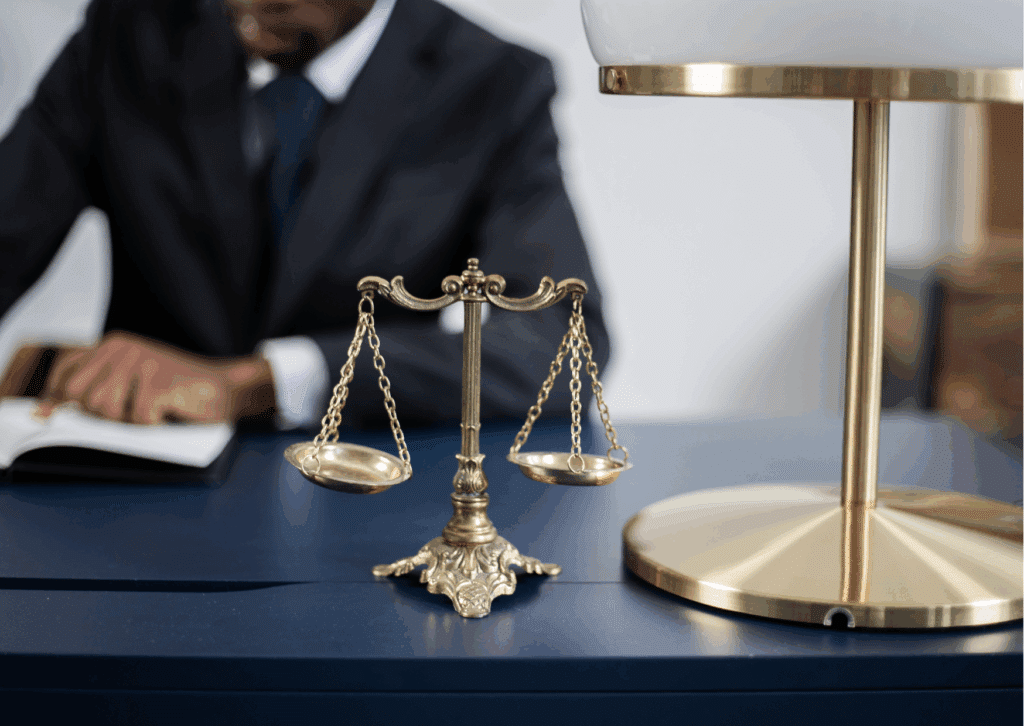 Balança da justiça sobre mesa de escritório com advogado ao fundo. Ilustração conceitual de arbitragem e mediação online como métodos jurídicos alternativos.